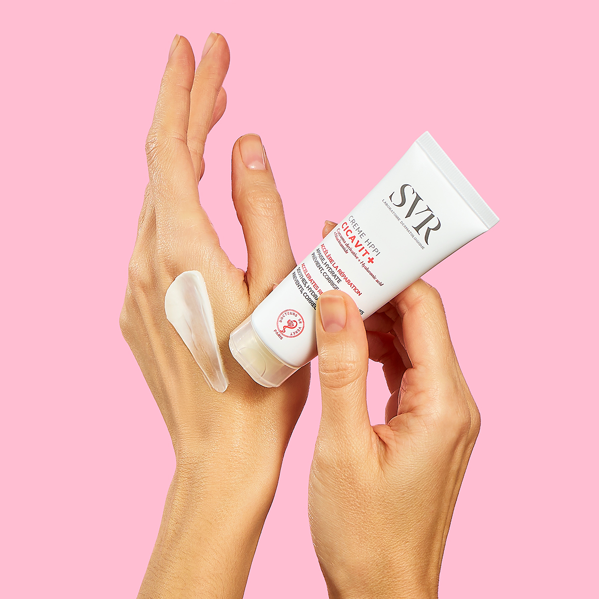 SVR CICAVIT+ Crème HPPI white tube being applied to skin, showing a smooth, creamy texture against a pink background.