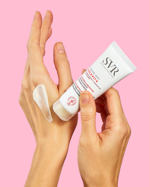 SVR CICAVIT+ Crème HPPI white tube being applied to skin, showing a smooth, creamy texture against a pink background.