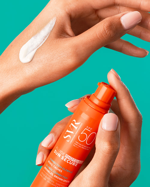 SVR Sun Secure Photo-Age SPF50+ Fluid in einer orangefarbenen Pumpflasche, aufgetragen als weiße Creme auf dem Handrücken.