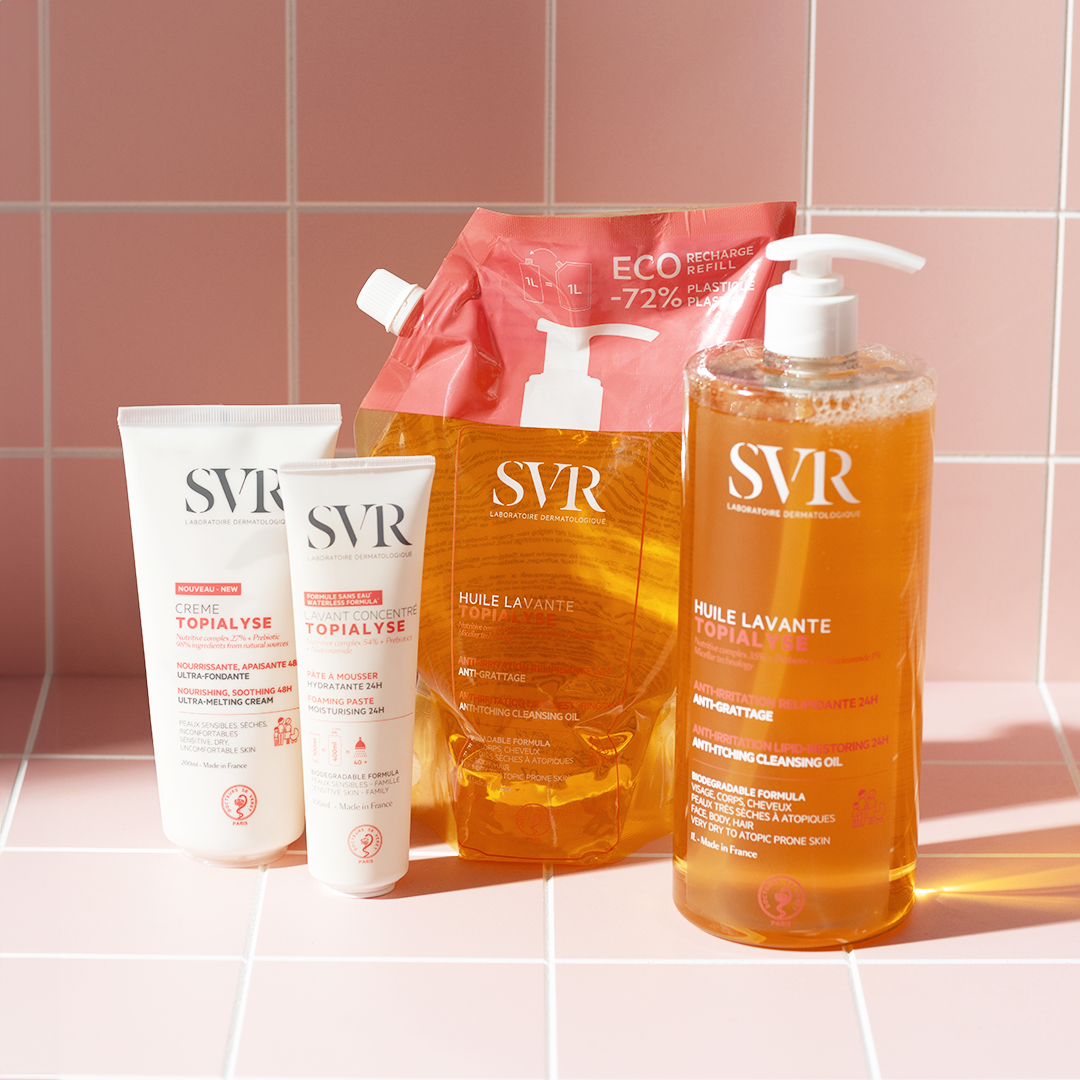 SVR Topialyse skincare collection featuring cleansing oils, refill pouch, and cream tubes on a pink tiled background.
