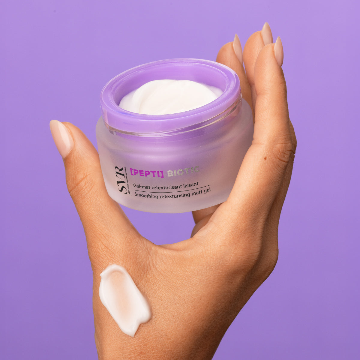 Hand holding a frosted glass jar of SVR PEPTI Biotic smoothing matt gel with a dollop of white cream on the skin.