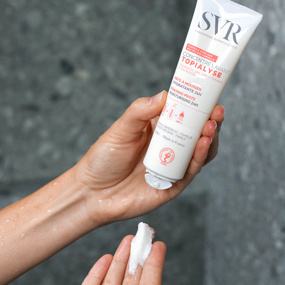 Hand holding a white tube of SVR TOPIALYSE Concentré lavant, dispensing a creamy white foaming paste into the palm.