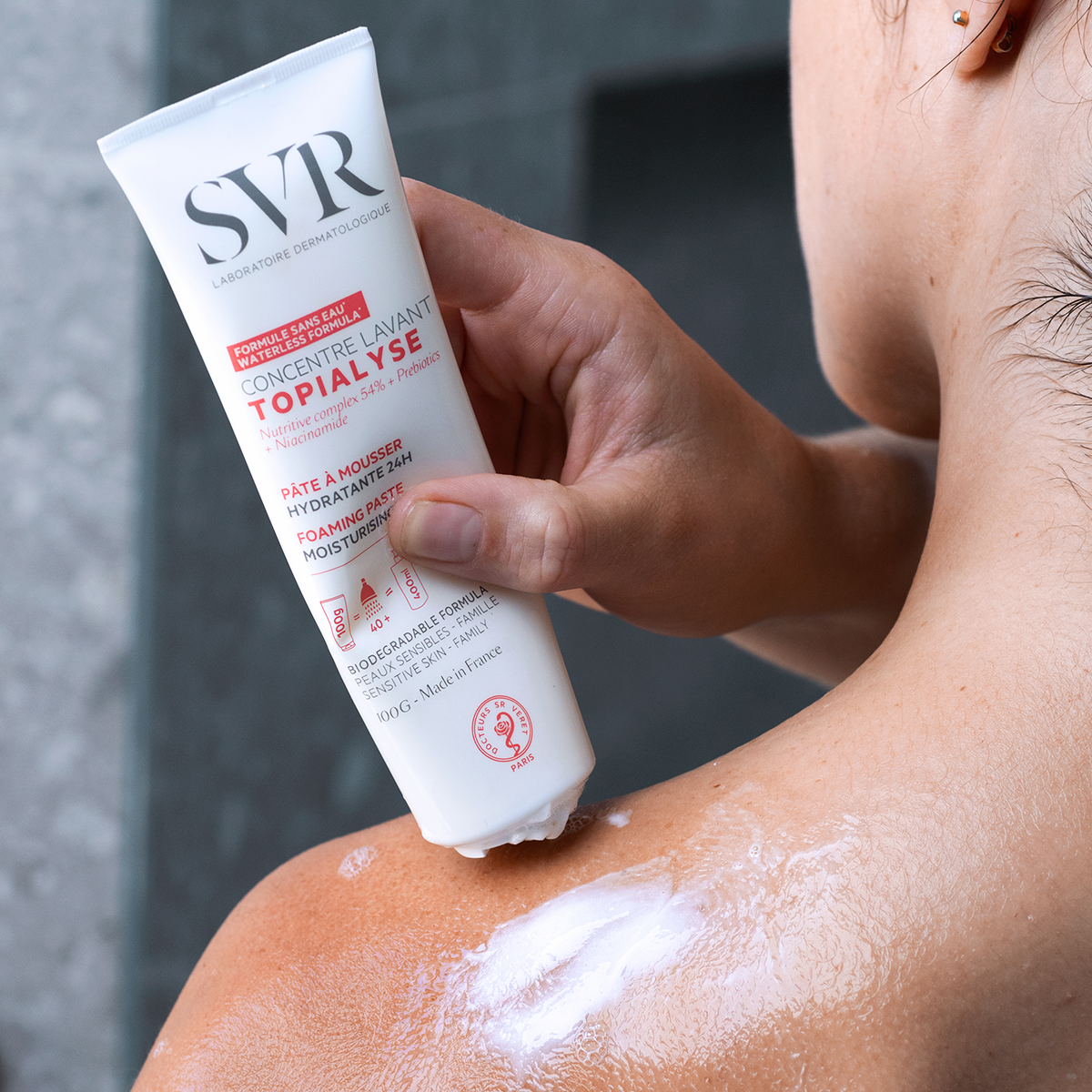 SVR TOPIALYSE Concentré lavant white 100g tube being applied as a foaming paste to a person's shoulder.
