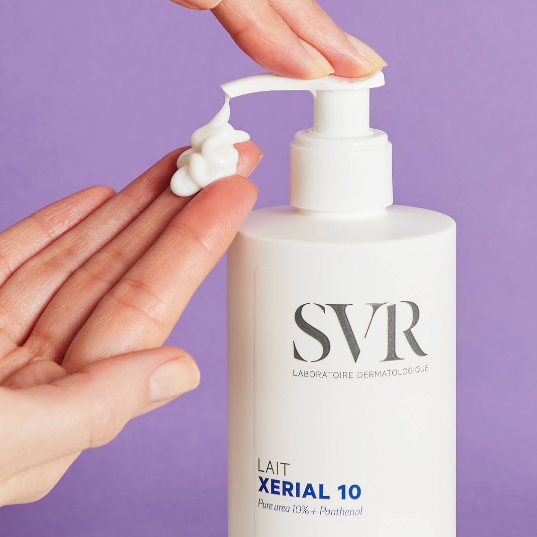 White SVR XERIAL 10 pump bottle dispensing thick white moisturizing cream onto a hand against a purple background.